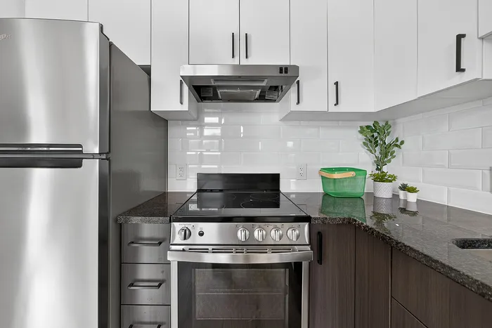 Modern kitchen with sleek stainless steel appliances, glossy white cabinets, and elegant dark countertops accented by a stylish black stove and fresh plant decor.