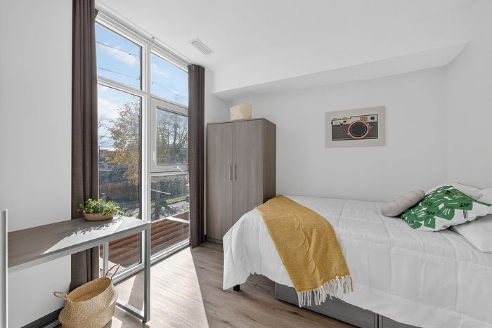 Bright bedroom with a large window, cozy bed, stylish decor, and modern furniture offering an inviting and serene space.