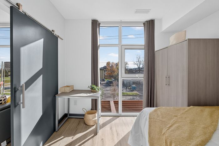 Bright apartment bedroom featuring large windows, modern furnishings, and stylish sliding barn door.