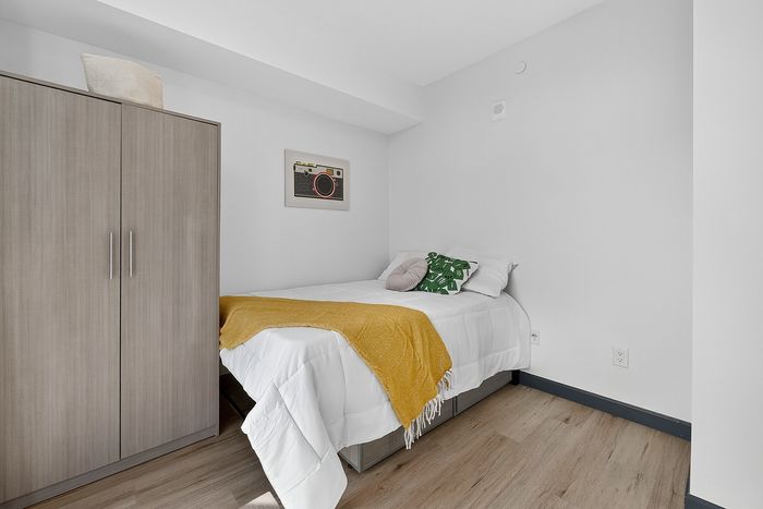Cozy bedroom featuring a stylish bed with crisp white linens and a vibrant mustard throw, complemented by modern decor and warm wooden flooring.