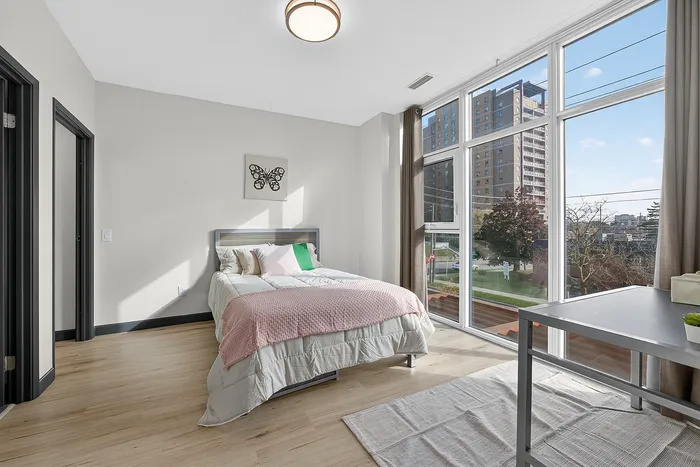 Bright and inviting bedroom with large windows offering stunning cityscape views, featuring elegant hardwood flooring and cozy modern furnishings.