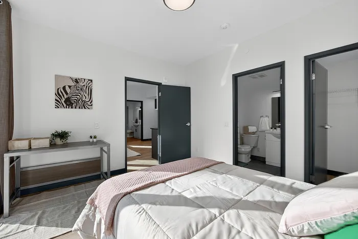 Elegant bedroom with stylish decor, featuring a cozy bed, chic artwork, and access to a modern bathroom and hallway.