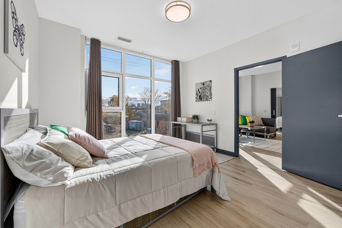 Sunlit modern bedroom with stylish decor, large windows, and a cozy seating area, offering a warm and inviting atmosphere.