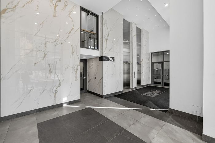 Elegant building lobby featuring marble walls, modern elevators, and sleek tile flooring.