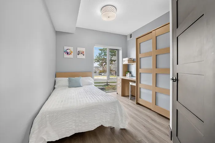 Bright and modern bedroom with a cozy bed, stylish artwork, and a functional desk area, enhanced by natural light from large windows.