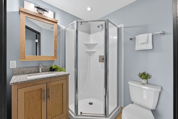 Contemporary bathroom featuring a sleek glass shower, elegant wooden vanity with granite countertop, and minimalistic decor.