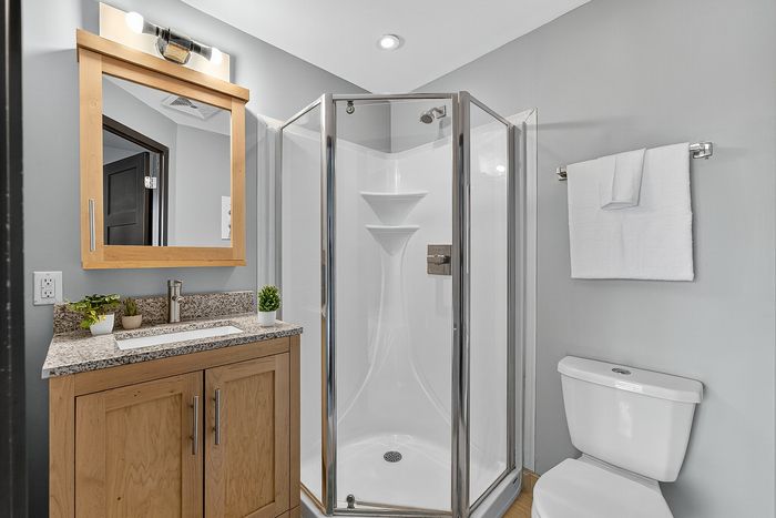 Modern bathroom with sleek corner shower, elegant wooden vanity with granite countertop, and stylish accessories.