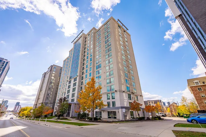 Modern high-rise apartment building with large windows and vibrant autumn trees, set against a clear blue sky.