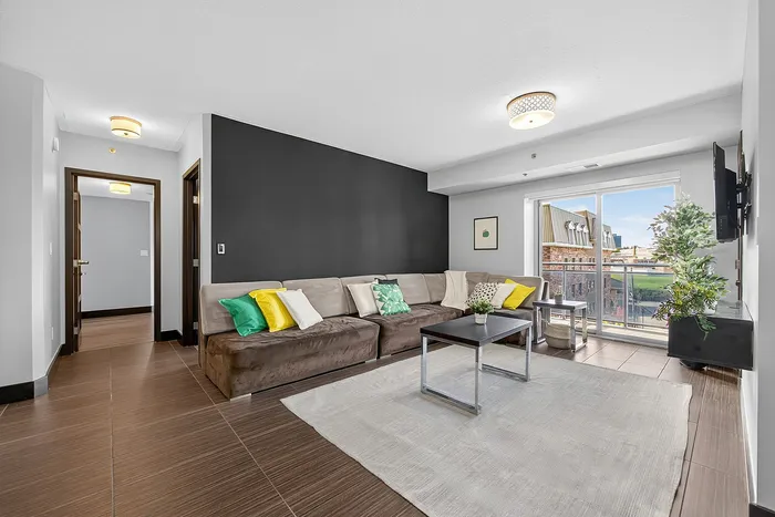 Modern living room with sleek brown sectional sofa, vibrant accent pillows, and a large window overlooking a scenic view.