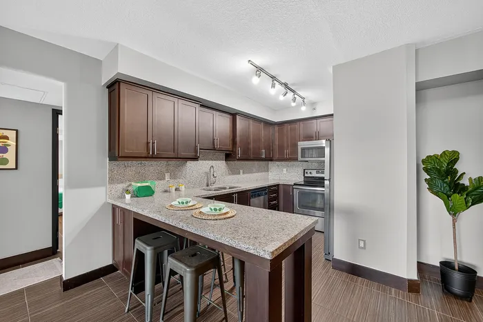Modern kitchen with elegant dark wood cabinets, sleek granite countertops, and stainless steel appliances, enhanced by stylish bar seating and ample lighting.