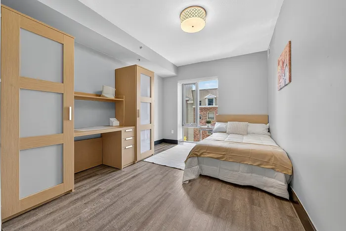 Bright, modern bedroom with sleek wooden flooring, stylish built-in storage, and a cozy bed by a large window offering an inviting view.