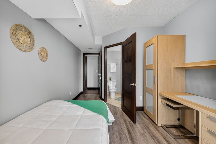 Modern bedroom with elegant hardwood floors, cozy bed, sleek wooden desk, and a stylish ensuite bathroom.
