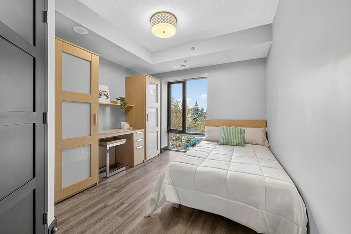 Bright and inviting modern bedroom with sleek wooden furniture, large window with scenic view, and a cozy bed in a serene setting.
