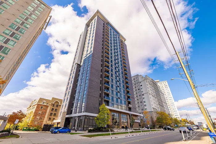 Modern high-rise apartment building with sleek glass windows, surrounded by a vibrant urban setting under a clear blue sky.