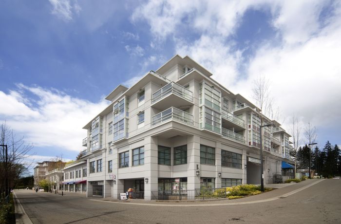 Modern apartment building with sleek balconies surrounded by a vibrant urban setting and blue sky.