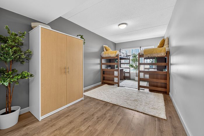 Modern bedroom with stylish loft beds, sleek wooden wardrobe, large window, and elegant potted plants offering a cozy and inviting atmosphere.