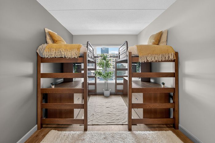 Charming bedroom featuring stylish wooden bunk beds, dual workspace with drawers, and a large window offering a bright city view.