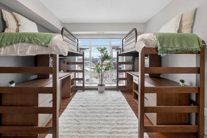 Modern and bright shared bedroom with lofted beds, large windows, and stylish wood furnishings, offering a cozy and spacious living area.