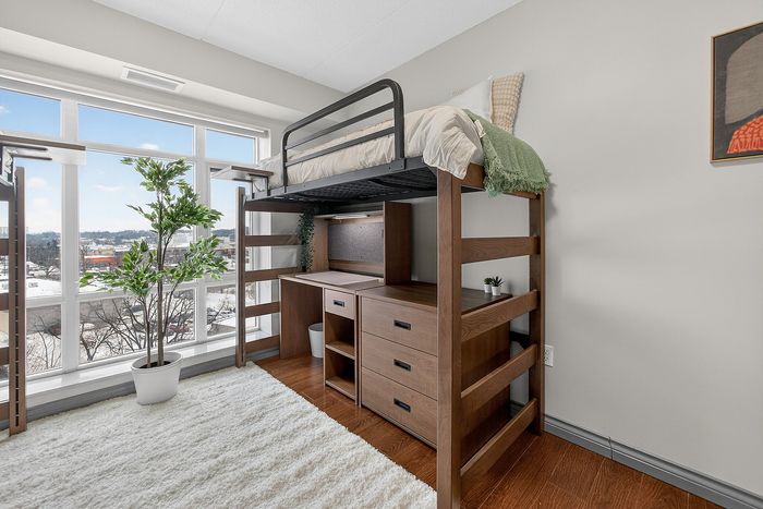 Modern bedroom with a sleek loft bed over a built-in desk and dresser, featuring a large window with scenic views and abundant natural light.