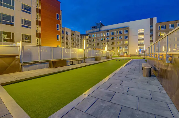 Modern apartment complex featuring a beautifully lit courtyard with a bocce ball court and stylish evening ambiance.