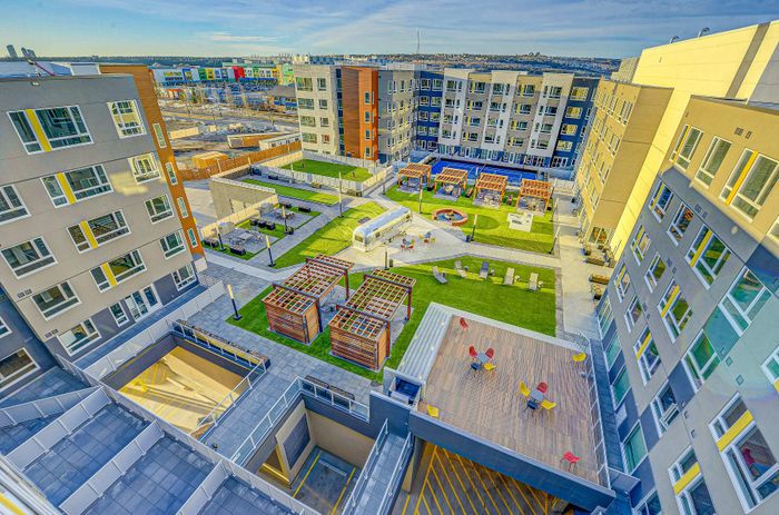 Vibrant apartment complex with modern architecture, featuring an inviting courtyard, lush green spaces, and colorful outdoor seating areas.