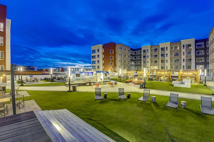 Vibrant apartment complex featuring a modern outdoor patio area with sleek seating, whimsical lighting, and inviting social spaces at dusk.