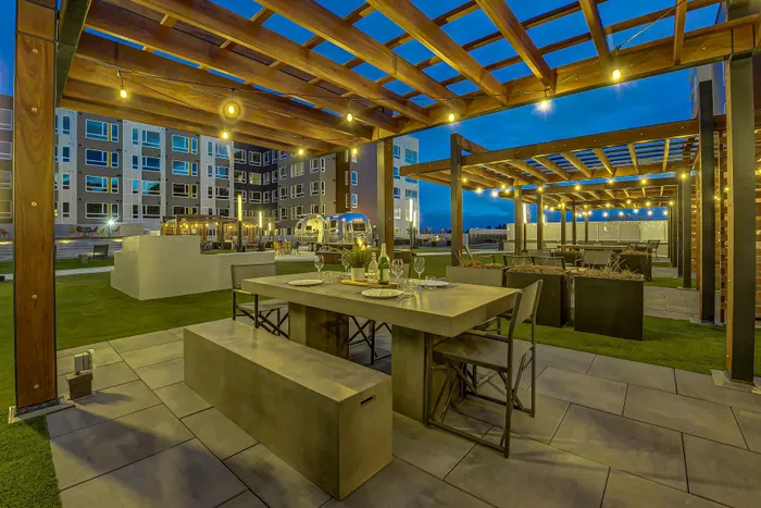 Chic outdoor dining area under ambient wooden pergolas with string lights, perfect for evening gatherings in a modern apartment complex.