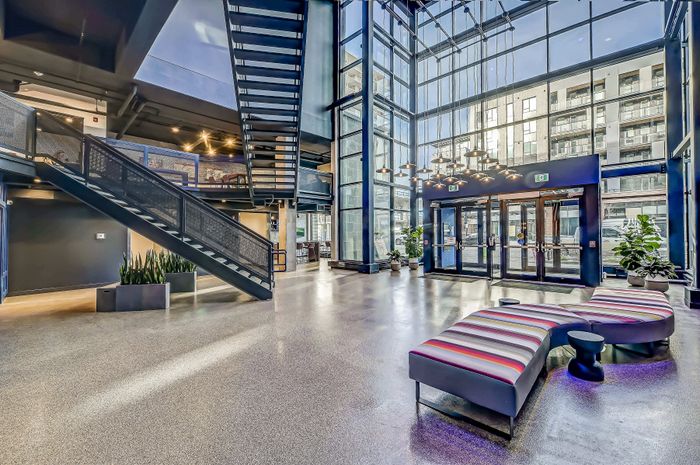 Modern apartment lobby with high ceilings, floor-to-ceiling windows, stylish lighting, and colorful seating.