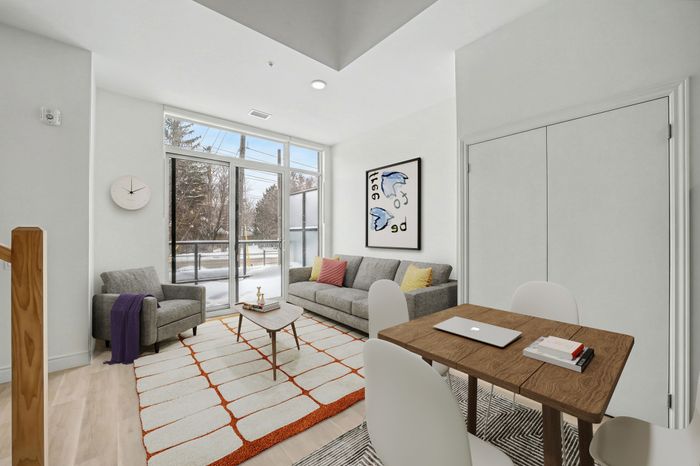 Bright and modern living room with large windows, stylish gray sofa, and elegant wooden dining table, perfect for a cozy and inviting atmosphere.