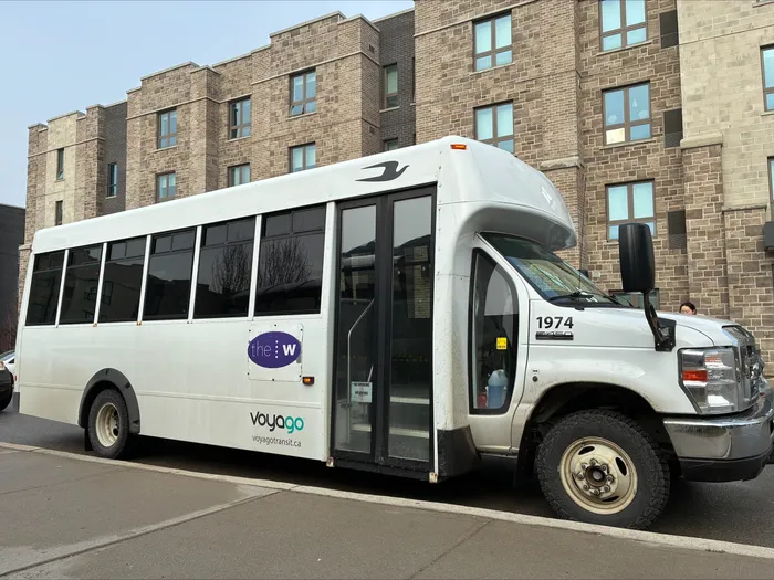Modern white shuttle bus parked in front of a contemporary brick apartment building, showcasing convenient urban transportation.