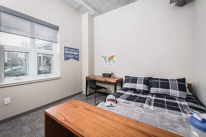 Cozy student room featuring a comfortable bed, study desk by a large window, and stylish decor.