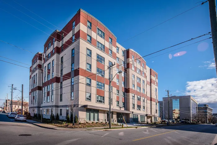 Modern urban apartment complex with a stylish red and beige facade, located on a bright, clear day.