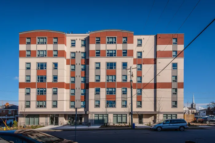 Modern apartment building exterior with sleek lines, large windows, and vibrant red accents against a clear blue sky.