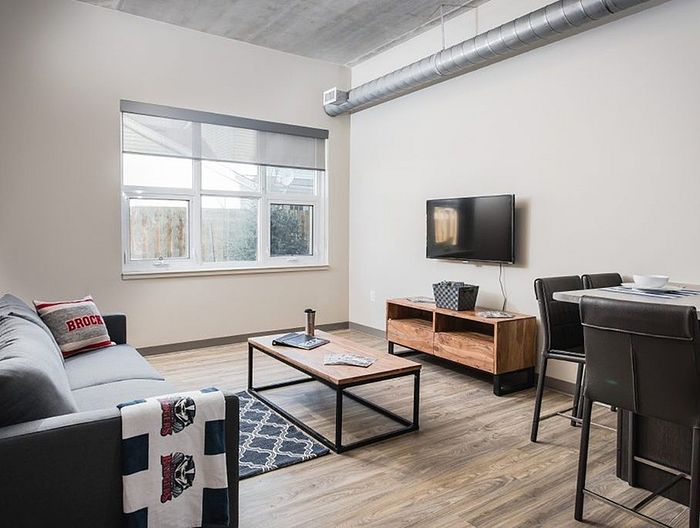 Modern living room with inviting sofa, stylish coffee table, wall-mounted TV, and chic dining area, featuring large window and sleek flooring for a cozy ambiance.