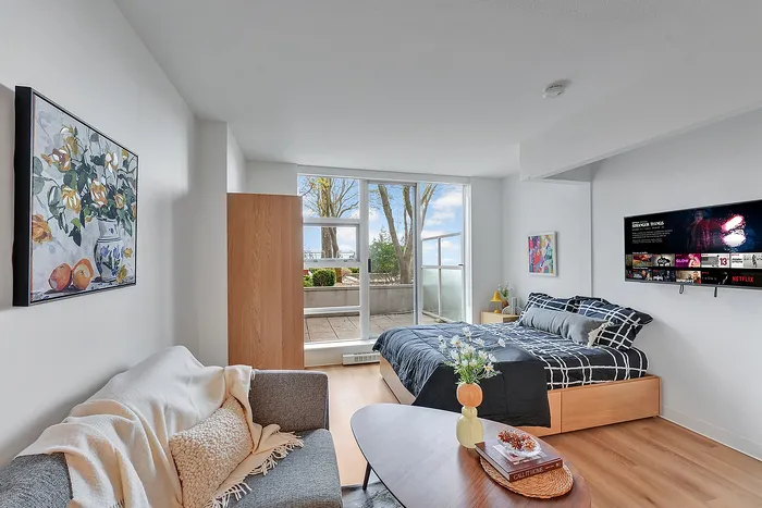 Modern studio apartment with cozy bed, stylish decor, and a bright view of the outdoor terrace.