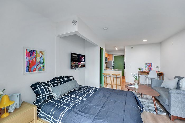 Modern studio apartment with stylish decor, featuring a comfortable bed, sleek kitchen with bar seating, and cozy living area.