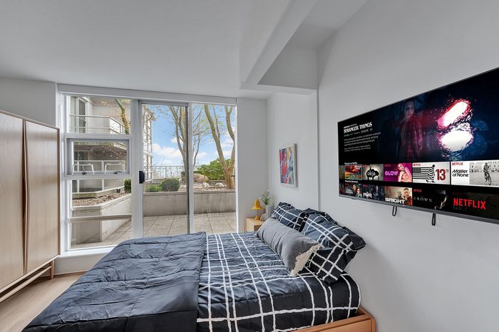 Modern bedroom with stylish decor, featuring a cozy bed, large flat-screen TV, and a bright view of a private patio through floor-to-ceiling windows.