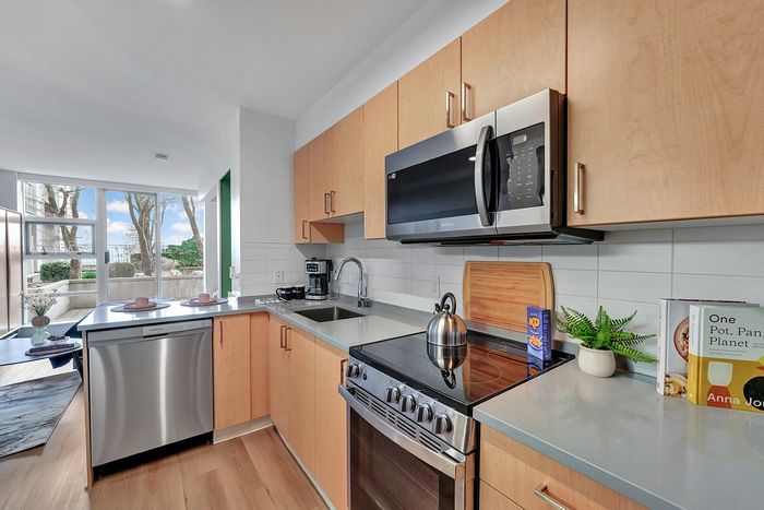Modern kitchen with sleek stainless steel appliances, elegant wooden cabinetry, and a bright view of the outdoors through large windows.
