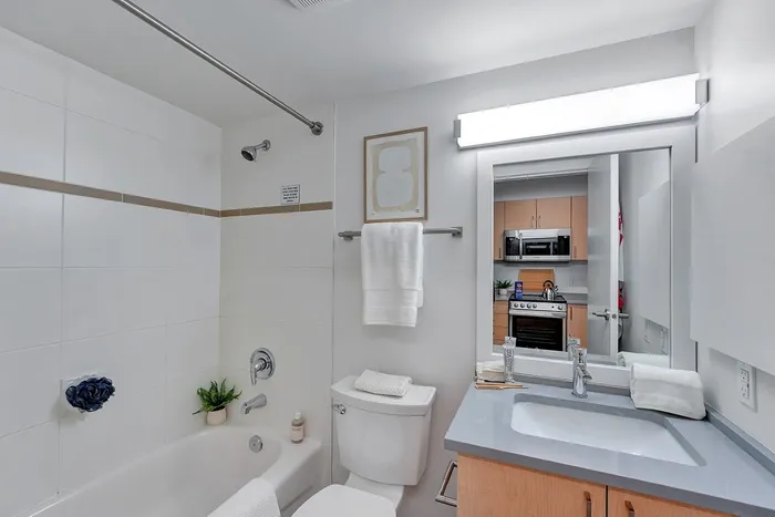 Modern bathroom featuring sleek fixtures, a spacious bathtub, and a stylish vanity with ample lighting, adjoined by a glimpse into a contemporary kitchen area.