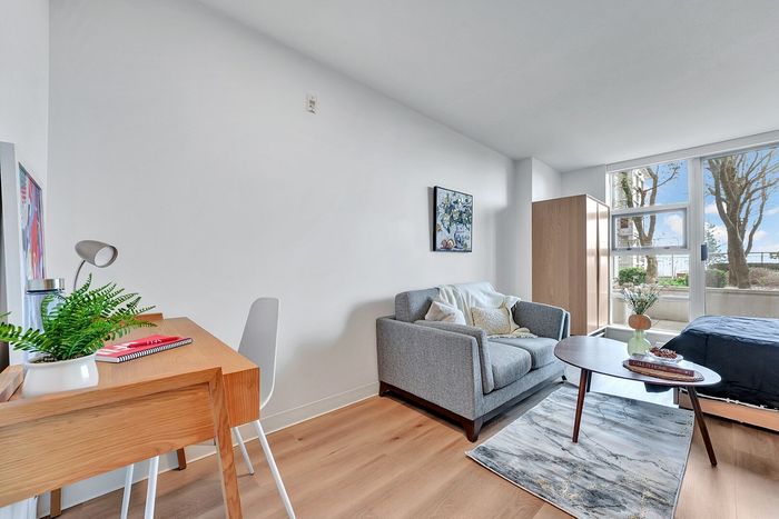 Bright and cozy apartment with a modern gray sofa, wooden desk, and large windows offering a scenic view.