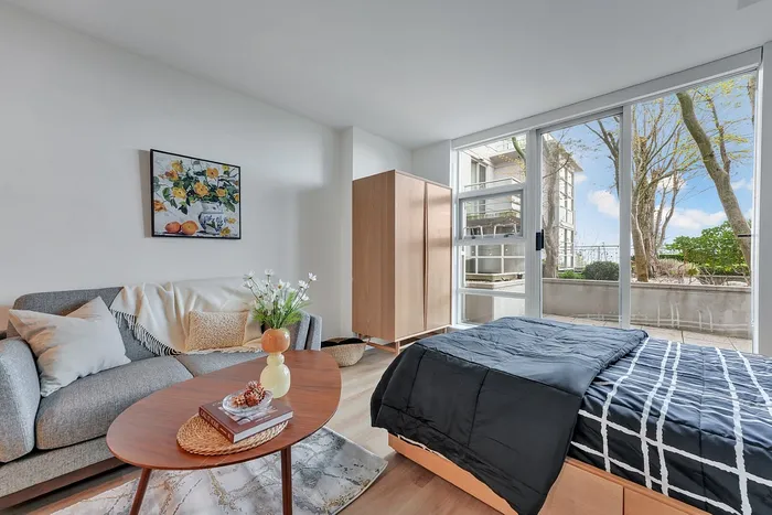 Bright apartment room with modern decor, featuring a cozy bed, stylish sofa, and large windows with a scenic view.