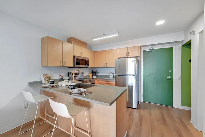 Modern kitchen with sleek cabinets, stainless steel appliances, and a stylish breakfast bar set for two accented by natural wood flooring.