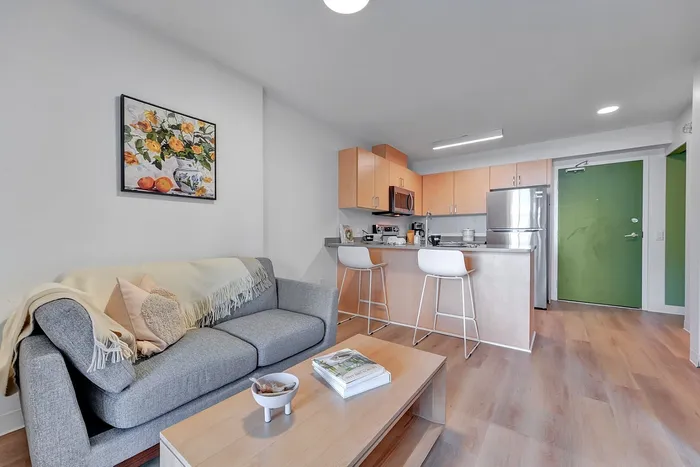 Charming apartment interior with a cozy gray sofa, modern kitchen with bar stools, and vibrant green entrance door, perfect for stylish urban living.