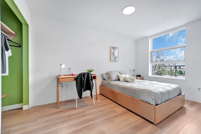 Bright bedroom with modern design featuring a cozy bed, wooden desk, and large window offering natural light and scenic views.