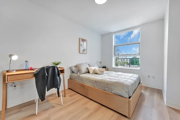 Bright and modern bedroom with large window, cozy bed, stylish wooden desk, and sleek hardwood flooring.