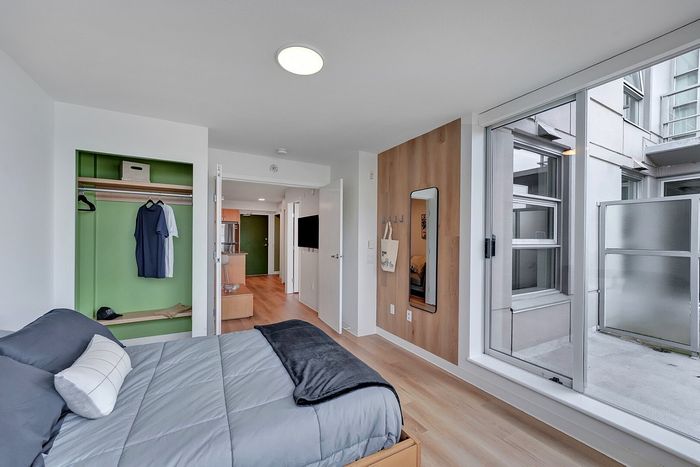 Modern and bright bedroom with sleek wood flooring, built-in wardrobe, and large window offering city views.