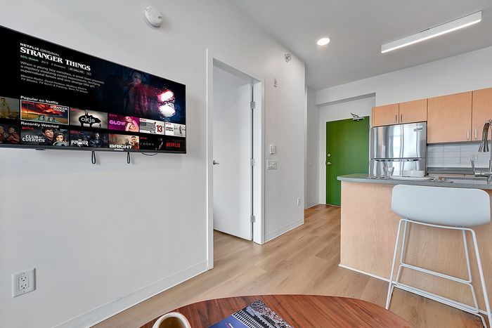 Modern apartment living area with sleek kitchen, vibrant green door, and mounted TV for an inviting and stylish atmosphere.