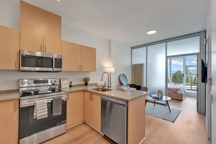 Modern open-plan kitchen with sleek stainless steel appliances, leading to a cozy living area and sunlit bedroom with mountain views.
