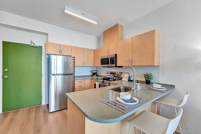 Modern kitchen with sleek stainless steel appliances, stylish wooden cabinetry, and elegant breakfast bar in a cozy apartment setting.