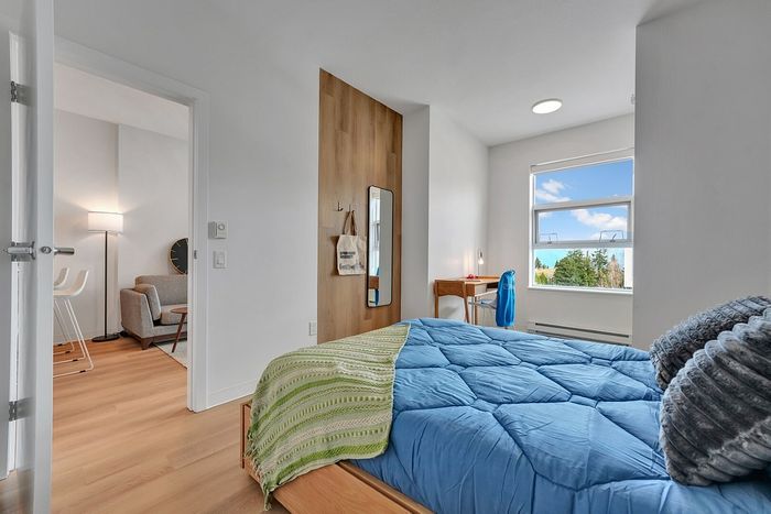 Bright and cozy bedroom with a stylish blue bedspread, modern wooden flooring, and a scenic window view. Adjacent to a chic living space featuring elegant furnishings.